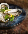 Assiette bleue avec des huîtres fraîches ouvertes garnies de persil et quartiers de citron sur lit de glace.