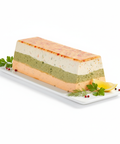 Terrine de poissons artisanale en couches colorées, servie avec citron et herbes fraîches sur assiette blanche.
