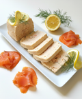 Terrines de poissons artisanales tranchées servies avec citron, aneth et saumon fumé sur plateau blanc, élégance et fraîcheur.