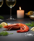 Gambas cuite bio servie avec citron et herbes fines sur table noire avec bougies et verres de vin blanc