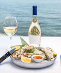 Plateau d'huîtres fraîches avec citron, sauces, verre et bouteille de vin blanc face à la mer, ambiance raffinée Les Huîtres