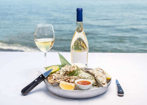 Plateau d'huîtres fraîches avec citron, sauces, verre et bouteille de vin blanc face à la mer, ambiance raffinée Les Huîtres