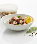 Fresh homemade salade de poulpe with lemon and herbs in white bowl and container behind on white background